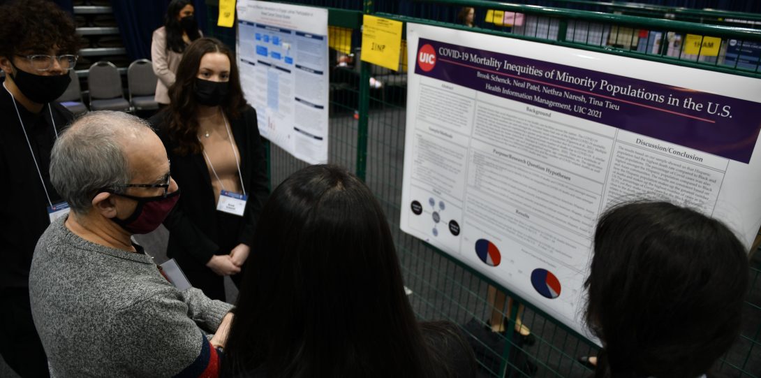 A student presents their research to several attendees at the 2022 Undergraduate Research Forum